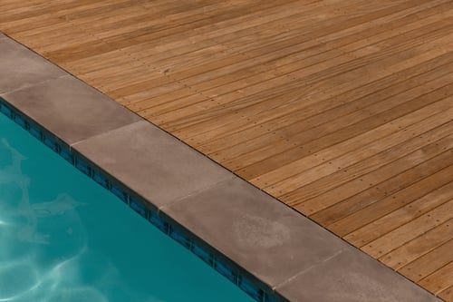 Sealed concrete pool deck edge meeting a timber deck surface