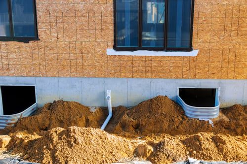 Foundation wall with window wells and fresh backfill on a residential build